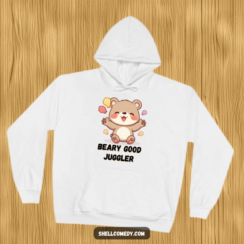 Funny bear cub hoodie juggling colorful seashells with delight, cozy beach apparel.